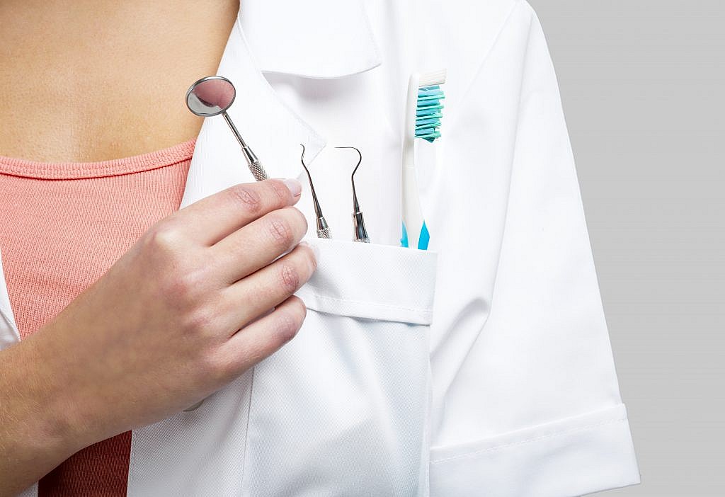 dentist in medical coat with toothbrush and other dental instruments in pocket